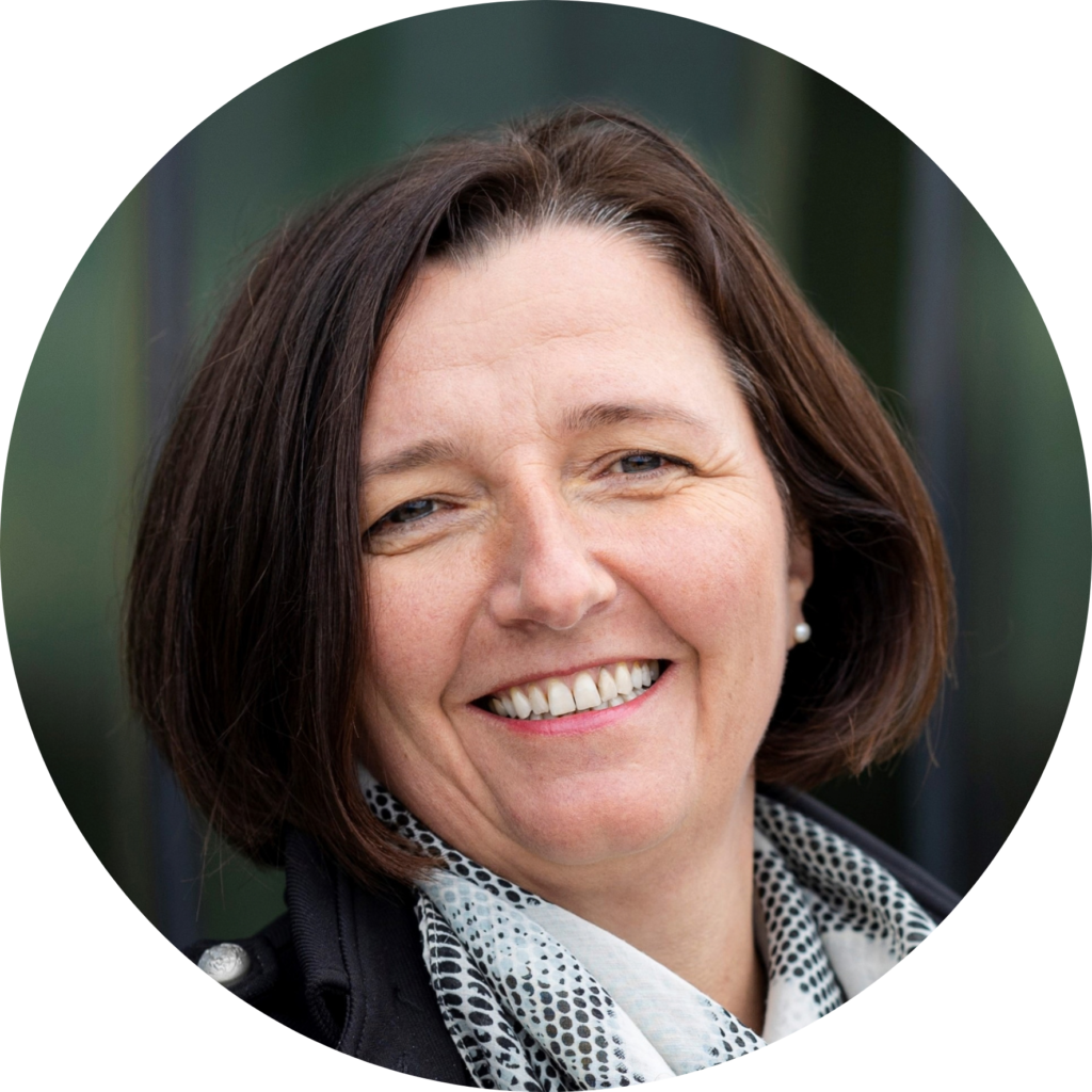 Portrait of Gitte Neubauer smiling, wearing a dark jacket and patterned scarf.